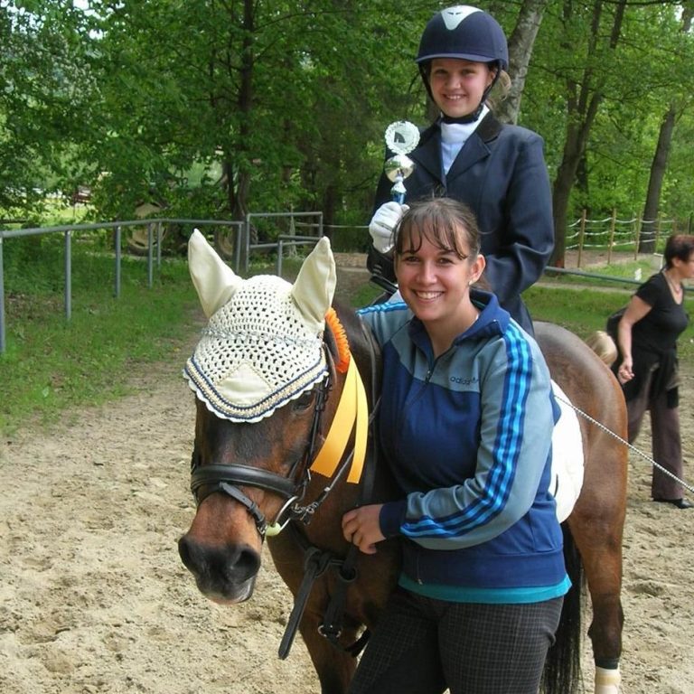 Braunes Pony mit Schleife und Reiter mit Pokal und Reitlehrerin auf Turnier